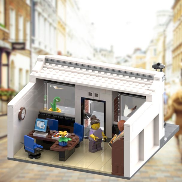 Modell eines Büros mit LEGO-Figuren, Möbeln und Computer in einer Straßenszene.